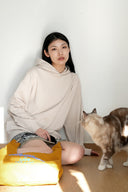 Model wearing Toby Black cream oversized hoodie with cat and yellow tote bag, sitting on floor with tabby cat