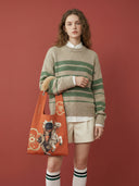 Model wearing Fortune Jockey Toby Bag with striped sweater and cream shorts against red background