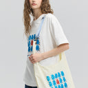 Model wearing a white t-shirt with colorful graphics, holding a cream-colored tote bag with similar designs.
