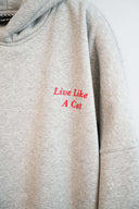 Front chest detail featuring red "Live Like A Cat" embroidery on light gray marl hoodie