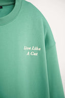 Close-up of cream "Live Like A Cat" embroidery on green