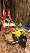 Dinner table with food, a drink, a toby cat keychain and tote bag on a wooden surface.