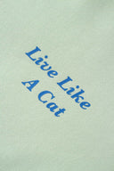Close-up of blue "Live Like A Cat" embroidery on green
