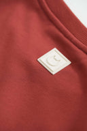 Back neckline detail featuring white leather cat logo patch on burgundy fabric