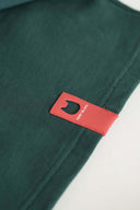 Red leather Toby Black cat logo patch on green sweatshirt hem.
