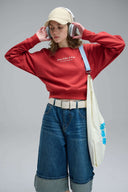 Toby Black sweatshirt styled look with model in rust-colored cropped jumper, wide-leg denim, cap and headphones