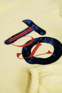 Close-up of velvet "TO By" embroidery on yellow hoodie