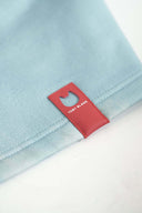 Close-up of red leather Toby Black brand tag with cat ear cutout on mint blue hoodie