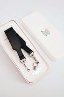 Black leather strap with silver hardware in a white box on a light gray background