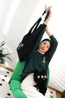 Model stretching with black tote bag wearing green sweatshirt.