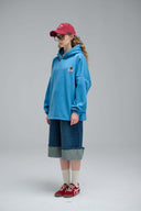 Side view of model in blue hoodie, red cap, and denim shorts.