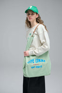 Model wearing a green cap and holding a light green tote bag with text.