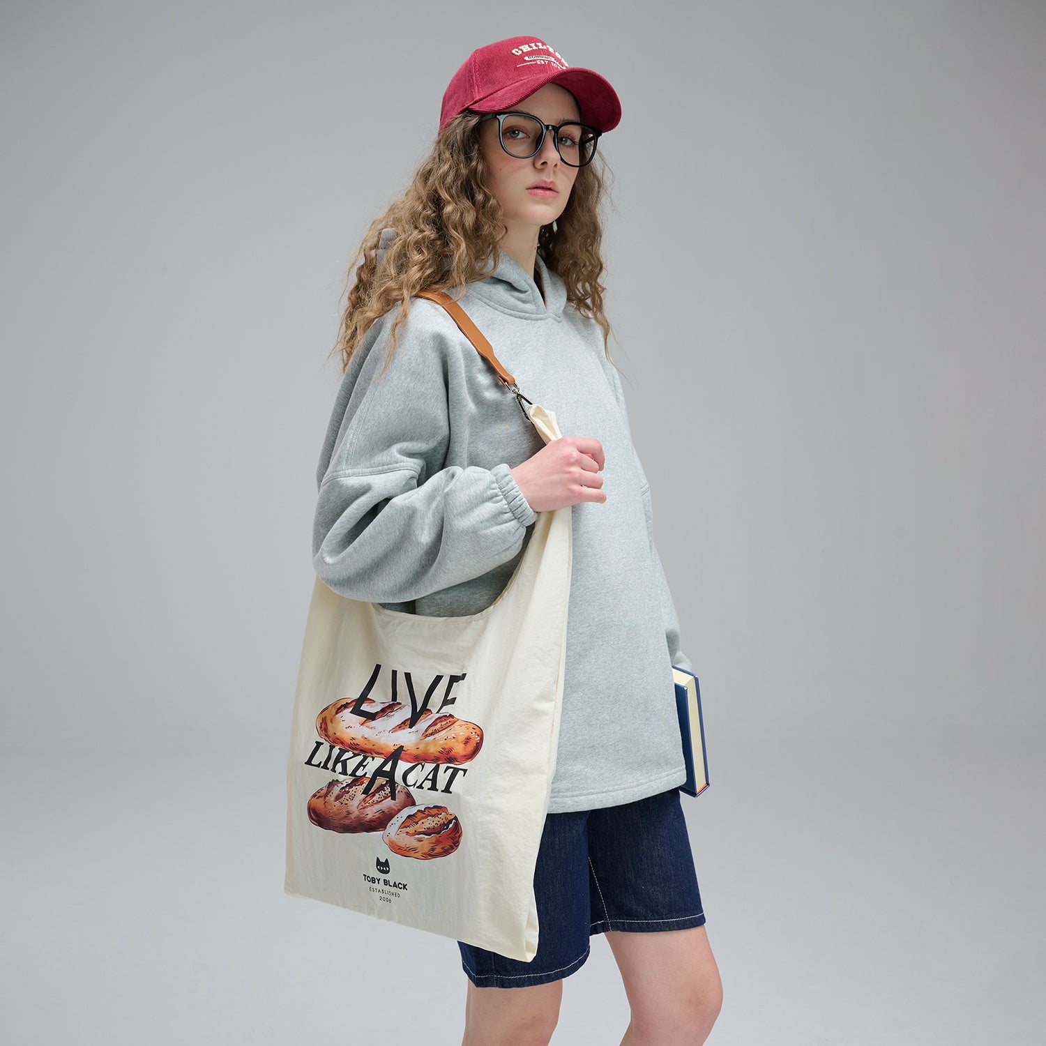 Person wearing a red cap and glasses holding a tote bag against a plain background.